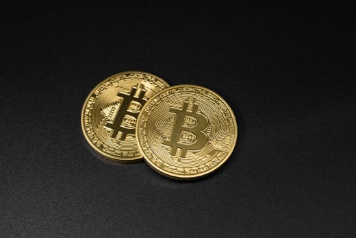 Two gold Bitcoin coins resting on a sleek black surface, symbolizing digital currency.