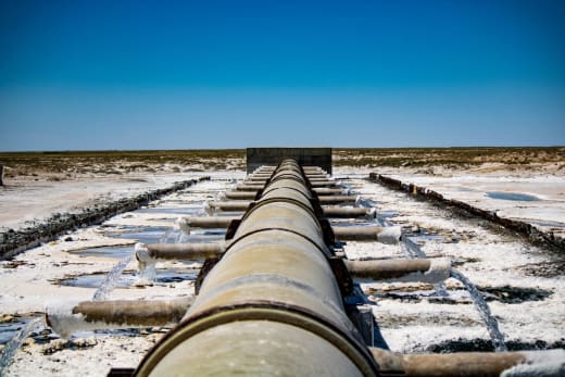 Large industrial pipeline discharging wastewater in arid, rural landscape under clear blue sky.