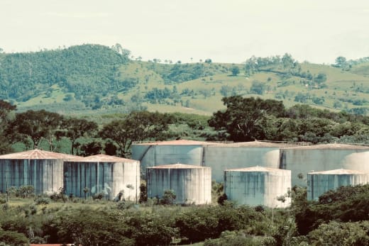 Large industrial storage tanks set amidst a verdant and hilly landscape.