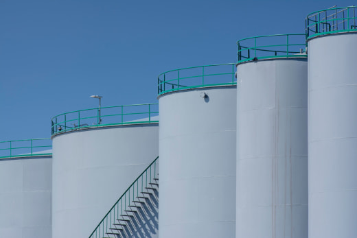Large industrial storage tanks with green railings against a clear blue sky.