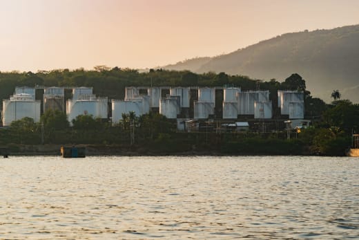 A picturesque view of industrial oil storage tanks set against a serene lake with mountains in the background.