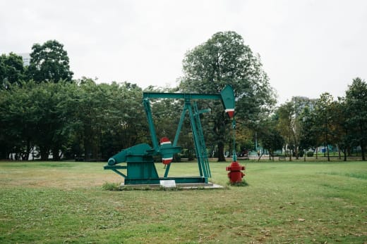 Green pumpjack in a Bangkok park, a fusion of industry and nature.