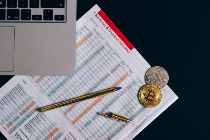 Top view of bitcoin coins on financial documents beside a laptop keyboard.