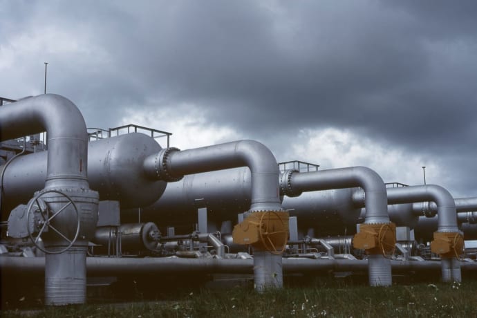 Gloomy industrial scene with metal pipes and valves under dark clouds.