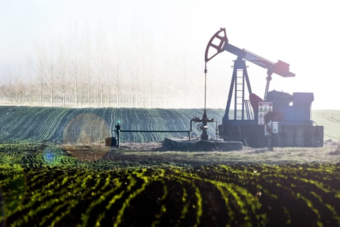 Oil pumpjack in scenic agricultural landscape with lush fields and distant trees.