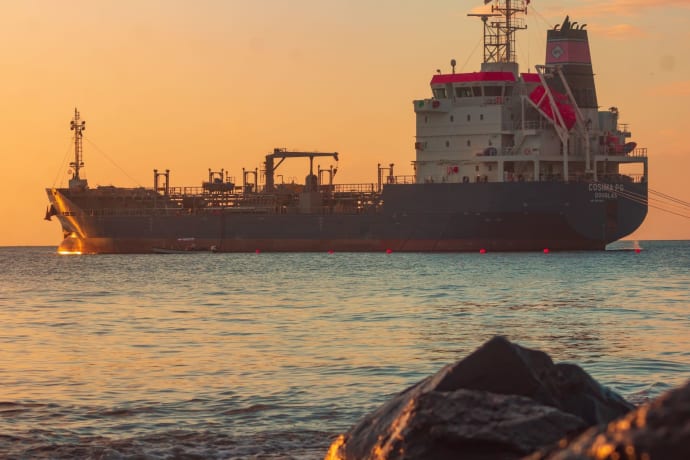 Large oil tanker on the ocean near the coast, sailing under a vibrant sunset sky.