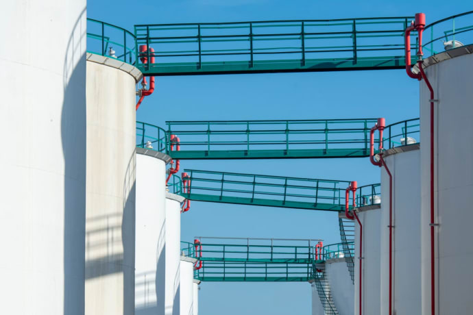 Modern industrial storage tanks with walkways against a clear blue sky.
