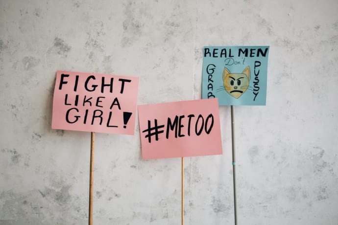 Signs displaying empowering feminist messages including "Fight Like a Girl" and "#MeToo," against a textured wall.