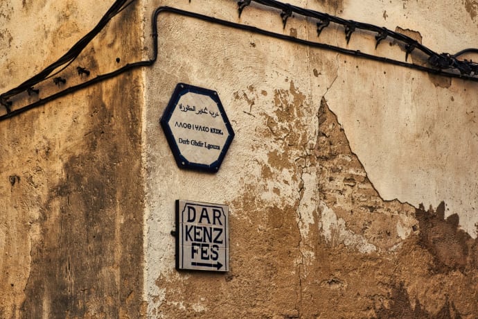 Street signs on a rustic wall in the medina of Fes, Morocco, showcasing cultural heritage.