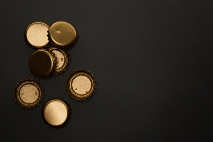 Flat lay of golden metallic bottle caps on a black background, offering copyspace.