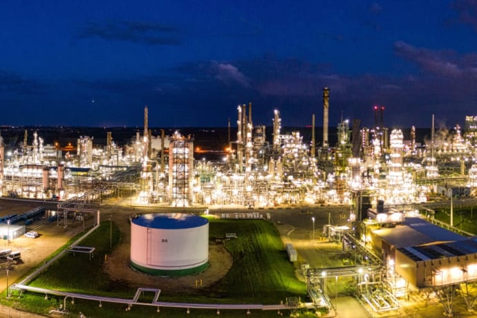Aerial night view of a brightly lit industrial oil refinery with smoking chimneys in Rosemount, MN, USA.