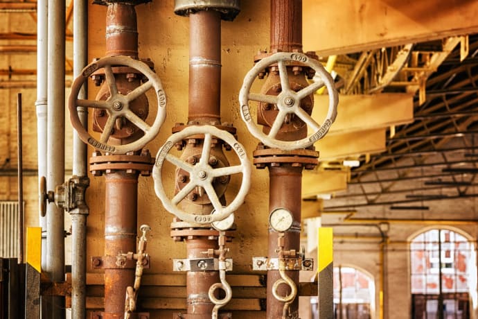 Close-up of rusty industrial pipes and valves, showcasing aging machinery in a factory setting.