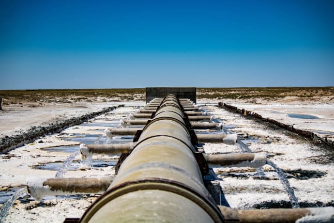Large industrial pipeline discharging wastewater in arid, rural landscape under clear blue sky.