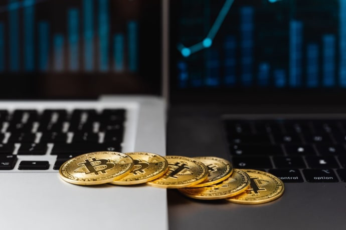 Gold bitcoins placed on laptop keyboards with digital financial graphs in the background.