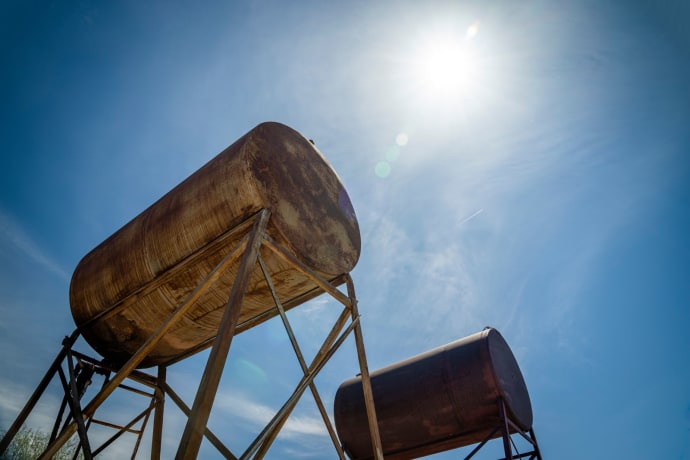 Rusty industrial oil tanks with a clear blue sky and bright sun.