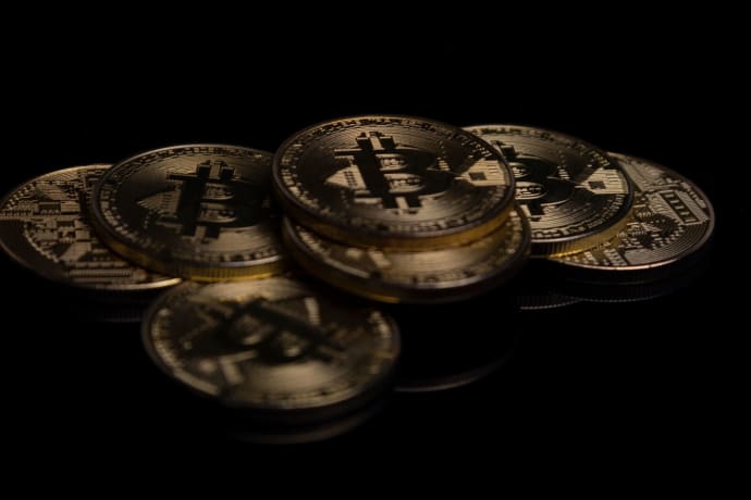 A close-up image of golden Bitcoin coins displayed on a reflective black surface.