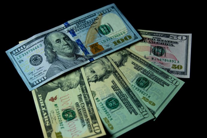 Detailed view of multiple US dollar bills against a black background, highlighting financial themes.