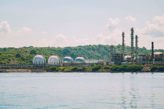 A scenic view of a coastal industrial gas storage facility with spherical tanks and tall chimneys.
