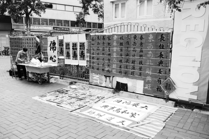 Grayscale photo of a street calligraphy stall in Hong Kong, showcasing Chinese characters.