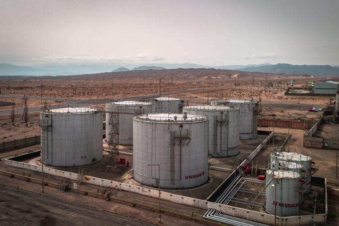 Aerial view of large industrial oil tanks in a desert setting with mountains in the distance.