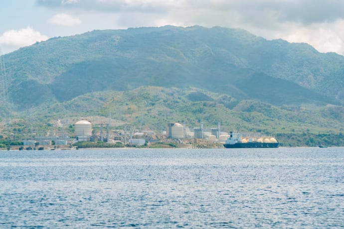 Coastal industrial facility with a tanker ship against a mountainous backdrop.