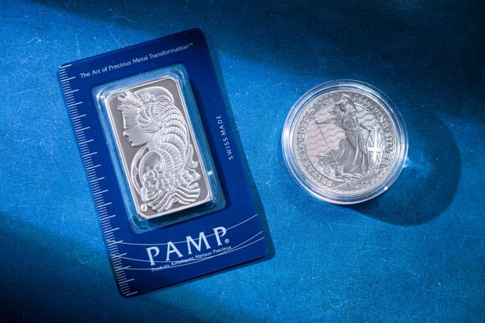 Close-up of a silver coin and a PAMP bar on a blue textured background emphasizing wealth.