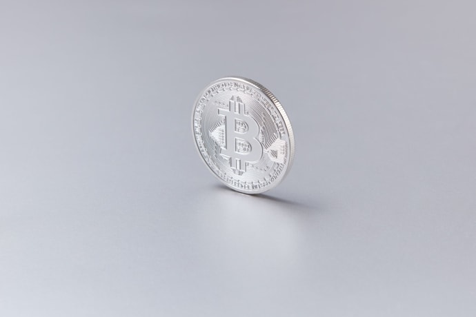 Close-up of a silver Bitcoin coin standing upright against a clean, white background.