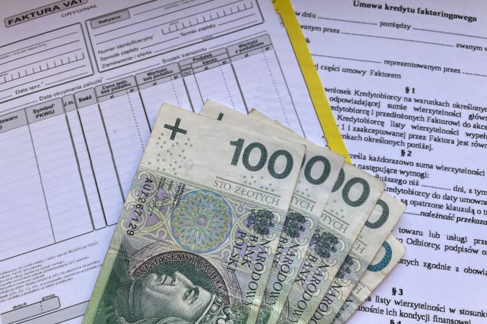 Polish 100 Zloty banknotes on VAT invoice and factoring agreement forms.