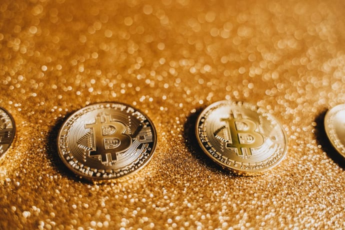 Three shiny Bitcoin coins on a glittery golden surface, symbolizing cryptocurrency and modern finance.