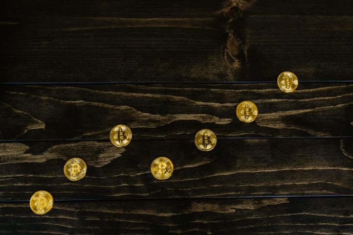 Gold-colored bitcoins arranged diagonally on a dark wooden surface.