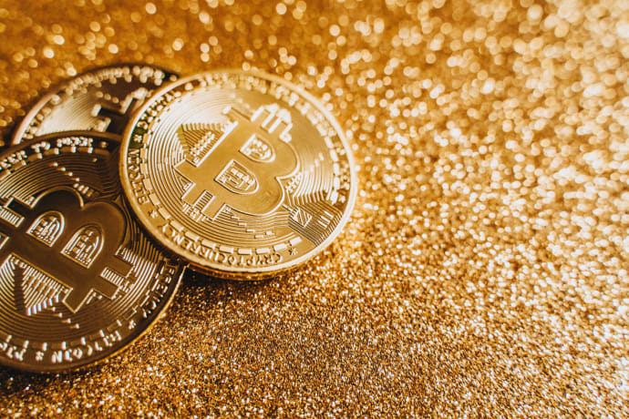 A close-up image of bitcoins placed on a sparkling gold glitter background, symbolizing cryptocurrency wealth.