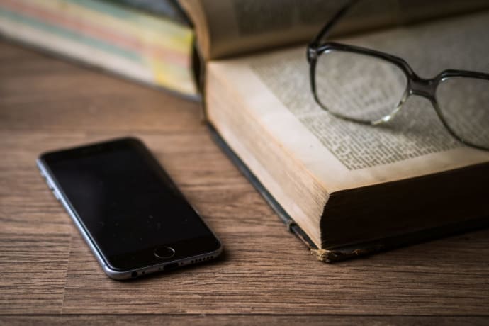 An open book, eyeglasses, and smartphone on a wooden desk, illustrating a classic study setting.