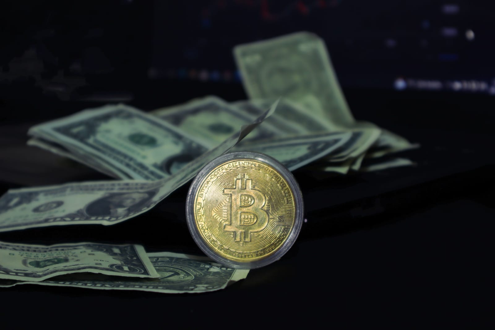 Bitcoin coin surrounded by scattered US dollar bills on a dark surface, symbolizing modern finance.