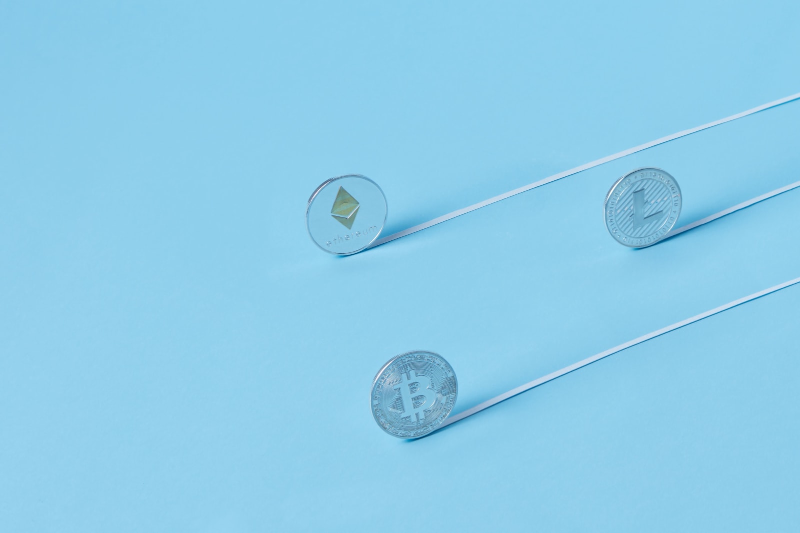Minimalist image of Bitcoin, Ethereum, and Litecoin coins on a baby blue background.