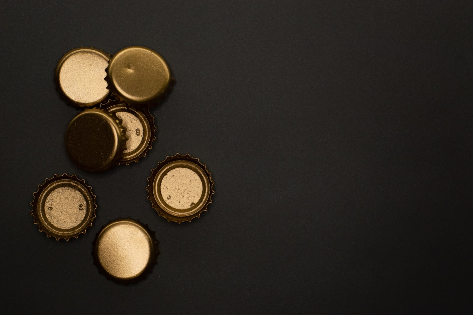 Flat lay of golden metallic bottle caps on a black background, offering copyspace.