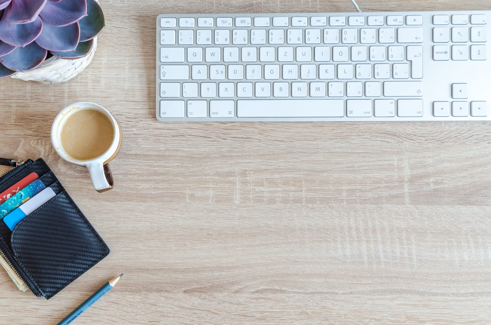 An organized workspace with a keyboard, coffee cup, wallet, and succulent plant on a wooden desk.