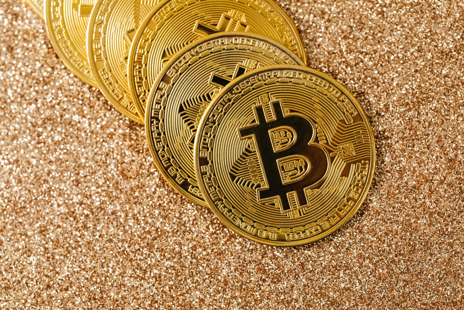 Golden Bitcoin coins arranged on a sparkling glitter surface, symbolizing cryptocurrency and wealth.