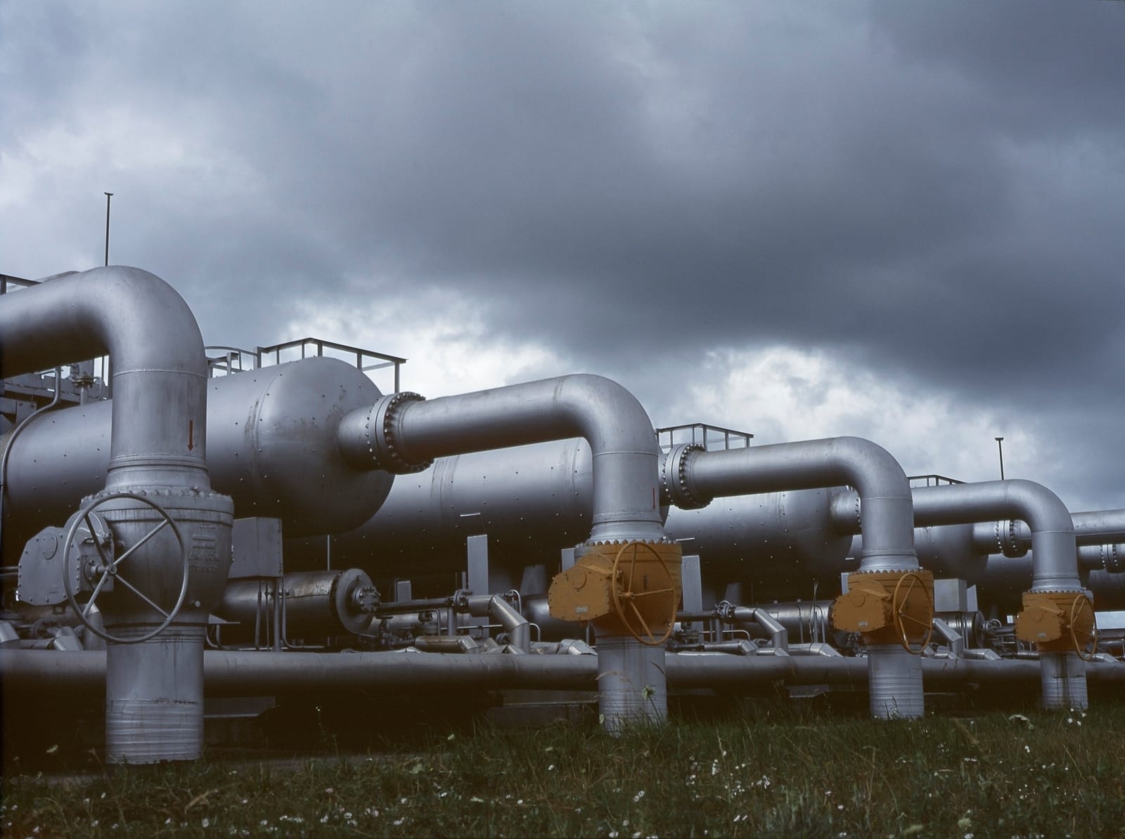 Gloomy industrial scene with metal pipes and valves under dark clouds.