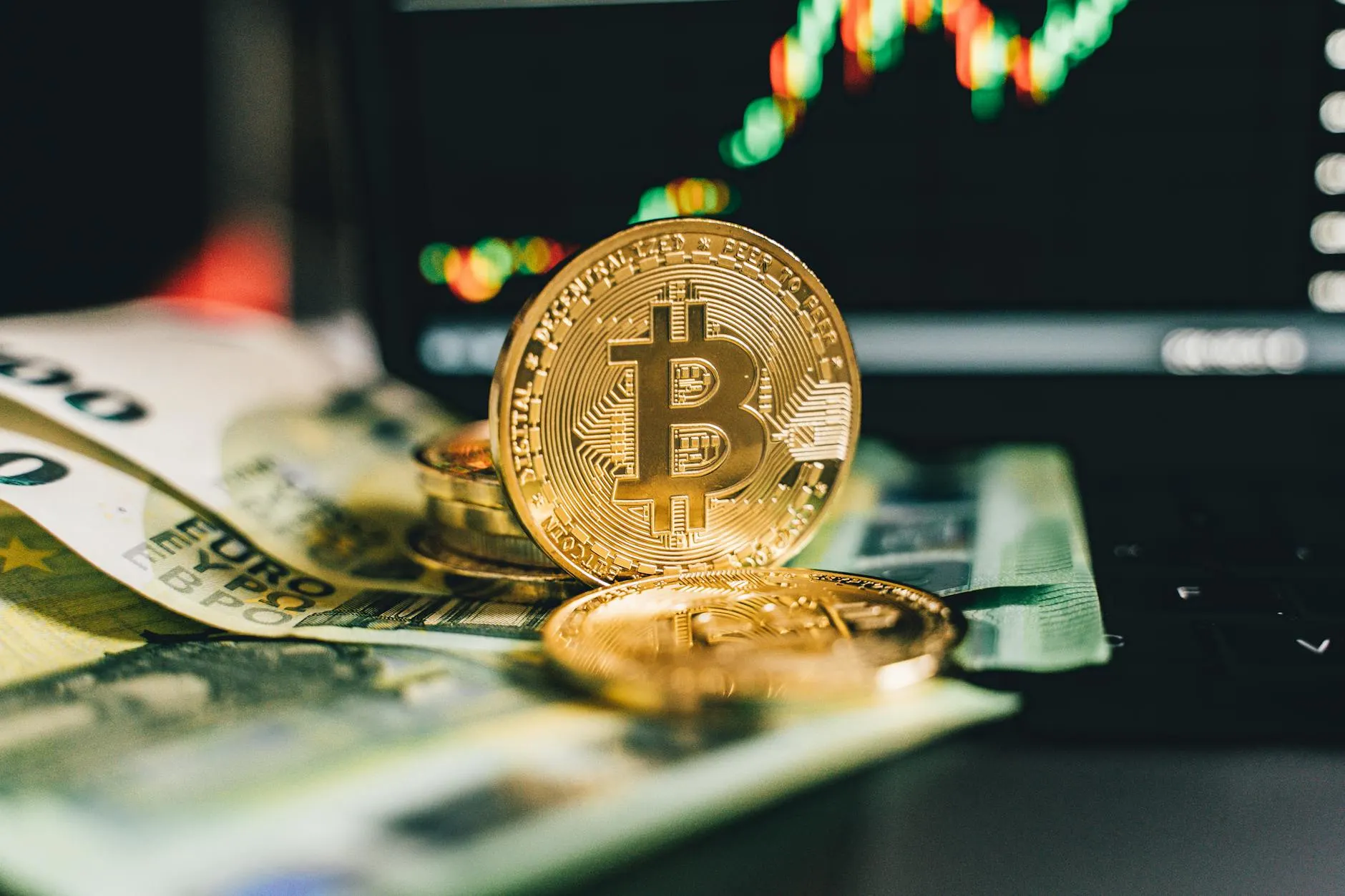 Close-up of Bitcoin and Euro notes on laptop keyboard with market chart in background.