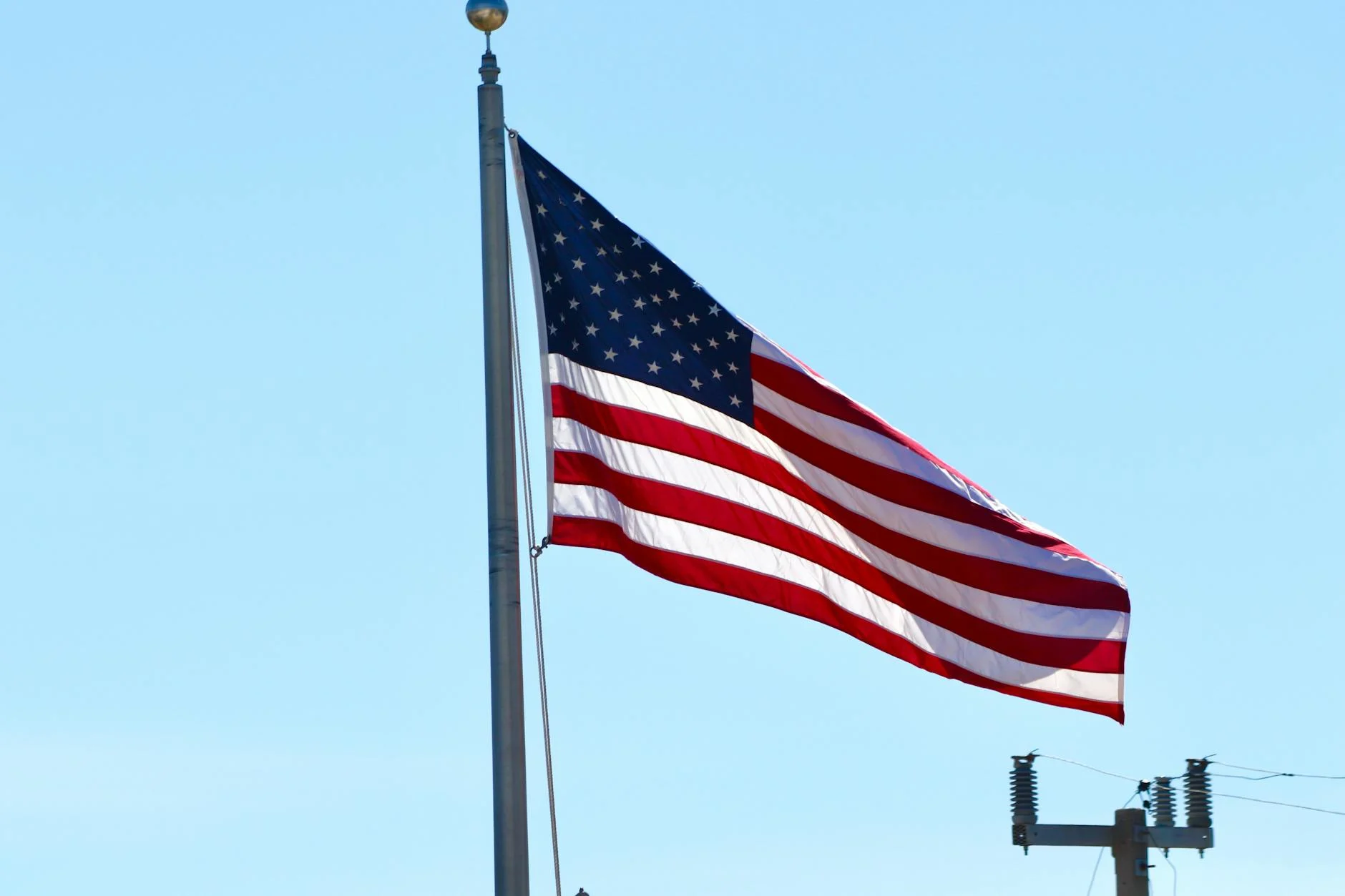 United States flag waving on a pole with a clear blue sky background in Florida.