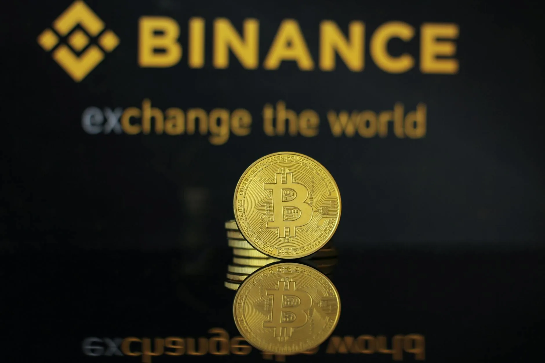 Close-up of a Bitcoin coin with Binance logo and text reflecting in dark surface.
