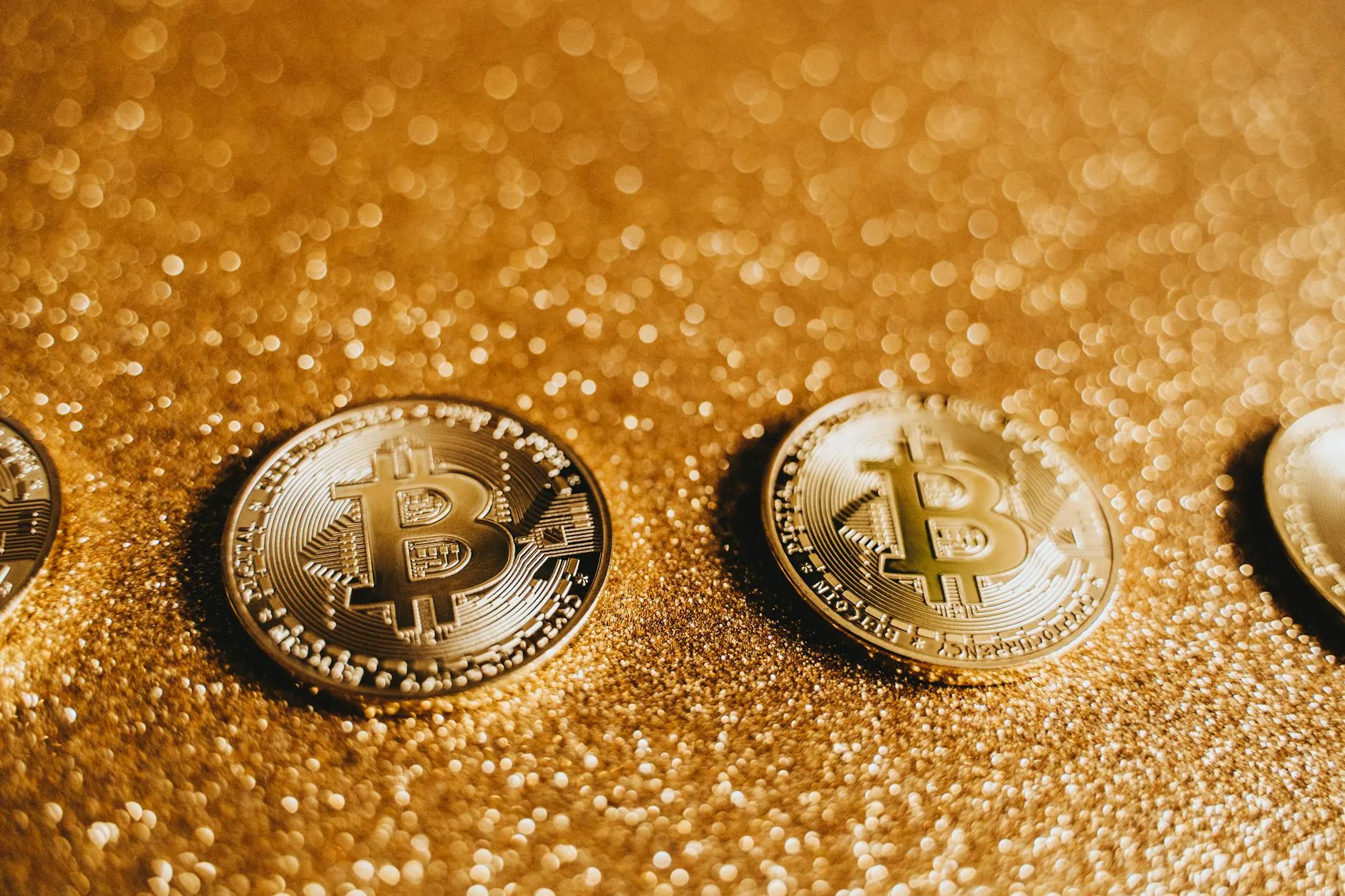 Three shiny Bitcoin coins on a glittery golden surface, symbolizing cryptocurrency and modern finance.