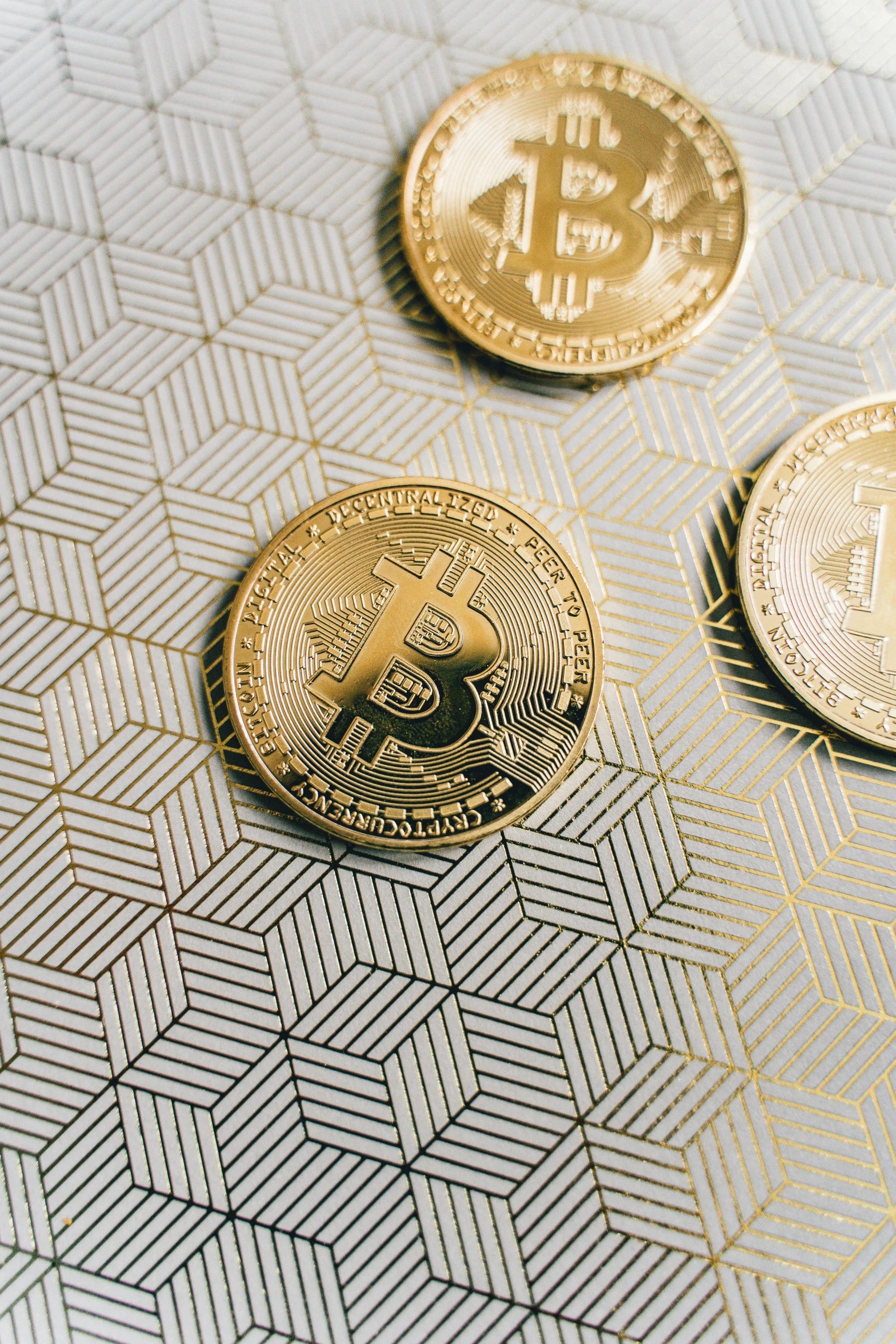 Three gold Bitcoin coins on a geometric patterned surface. Perfect for cryptocurrency content.