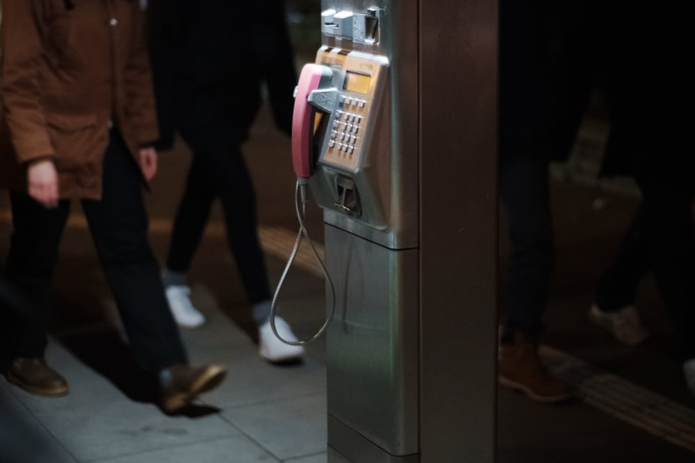 Phone booth at night time with two misterious people walking on each side of it