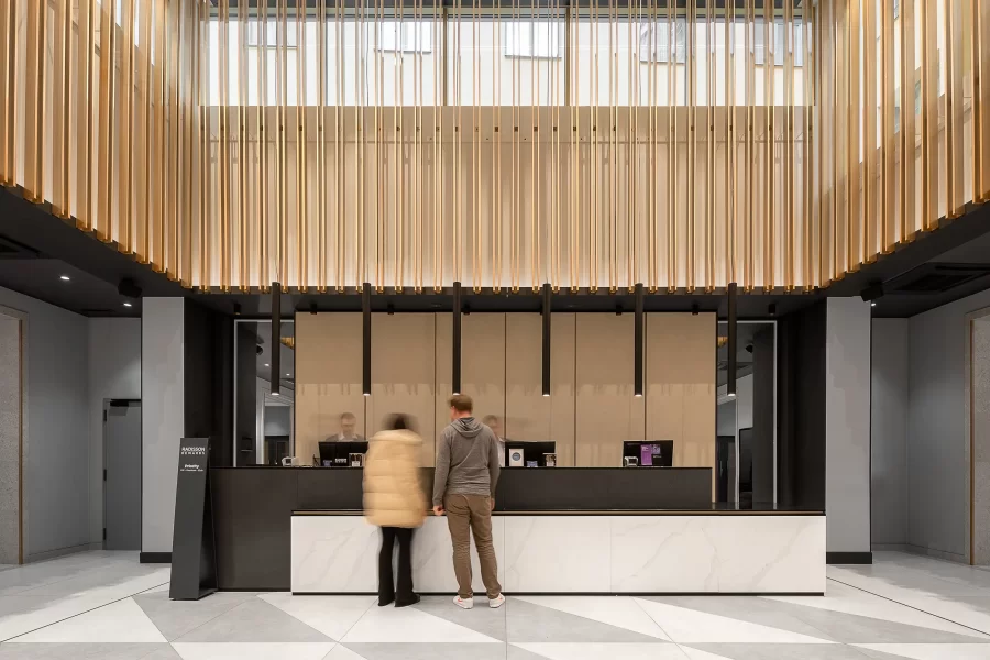 Die Frontalansicht der minimalistischen Rezeption des Radisson Blu Prag mit hohen Decken, goldenen Wanddekorationen und verschwommenen Gästen davor.