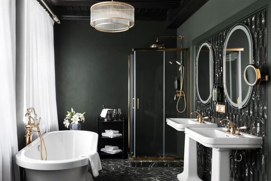 Luxurious and spacious castle hotel bathroom in dark green colour with solitary standing bathtub, shower and two washbasins.