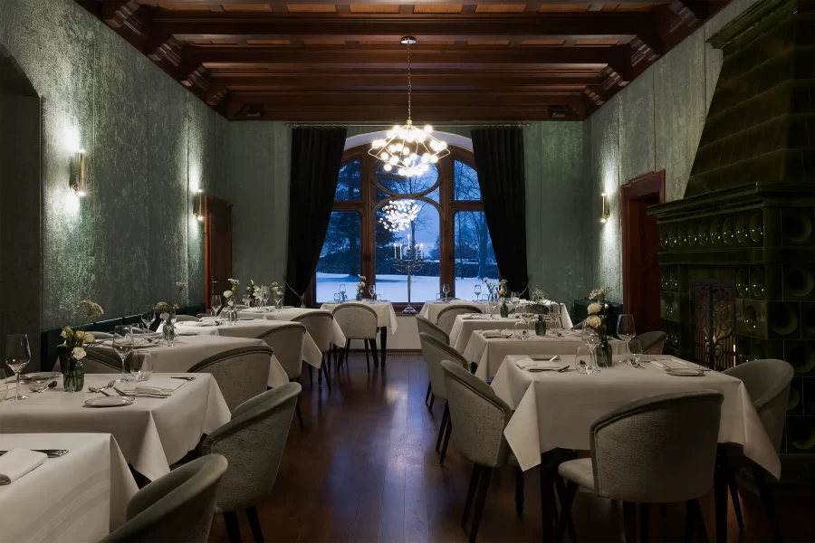 A dimly lit luxurious chateau restaurant with a prominent window with a snowy landscape behind it.