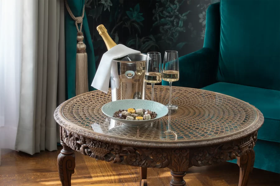 Detailaufnahme eines runden Beistelltisches in der Caspar-David-Friedrich-Suite im Schlosshotel Althörnitz mit Champagner, Gläsern und Suite-Interieur.