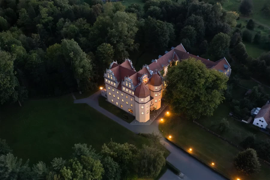 Luftaufnahme des Schlosshotels Althörnitz in der Dämmerung, umgeben von Waldlandschaft und dezent beleuchteten Wegen.