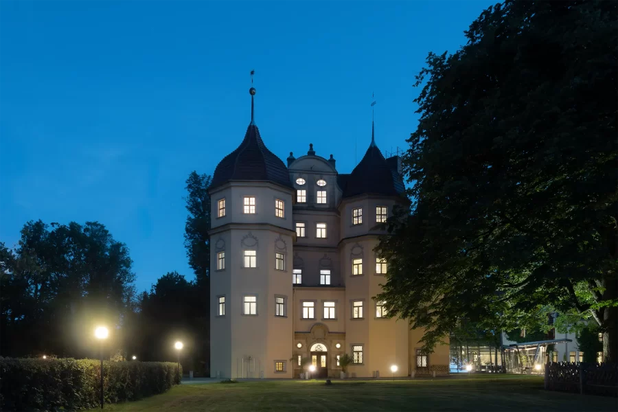 Frontalansicht des Schlosshotels Althörnitz zur blauen Stunde im Sommer, mit zentraler Perspektive und beleuchteter Fassade.